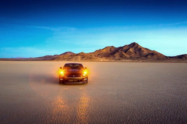Auto mit eingeschalteten Scheinwerfern in der Wüste