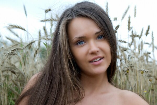 Una chica sonriente con el pelo largo de pie en un campo de trigo