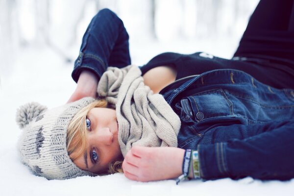 A girl in a hat is lying in the snow