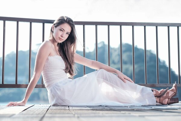 A girl in a white dress is sitting on the floor of the balcony