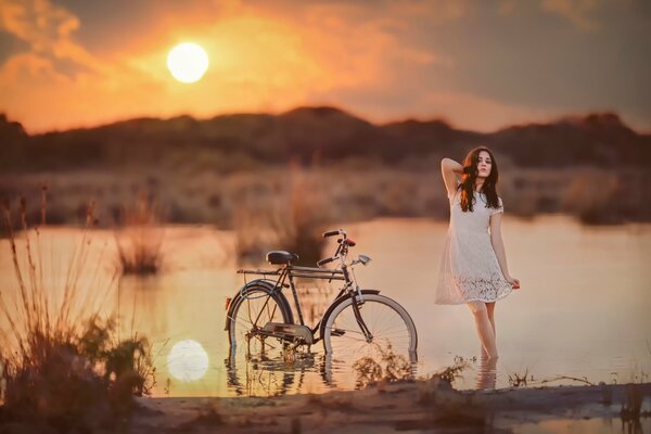 A girl with a bicycle on the shore of a pond