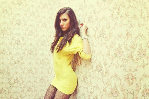 Levushka in a yellow dress poses against the background of ragged wallpaper