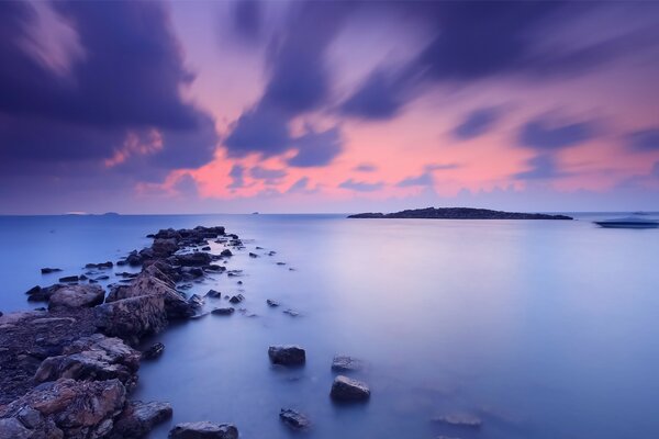 Piedras en el mar en medio de una puesta de sol naranja