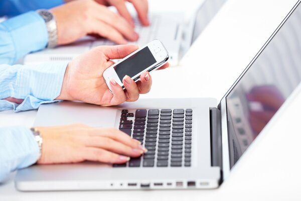 A woman holds her phone upside down and sits at her laptop