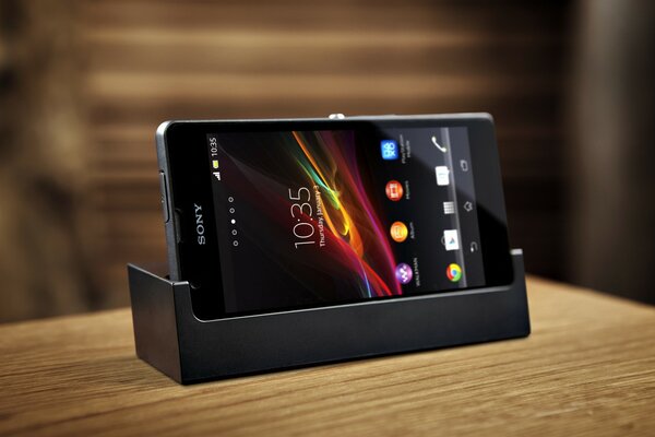 A sony xperia phone is charging on the table