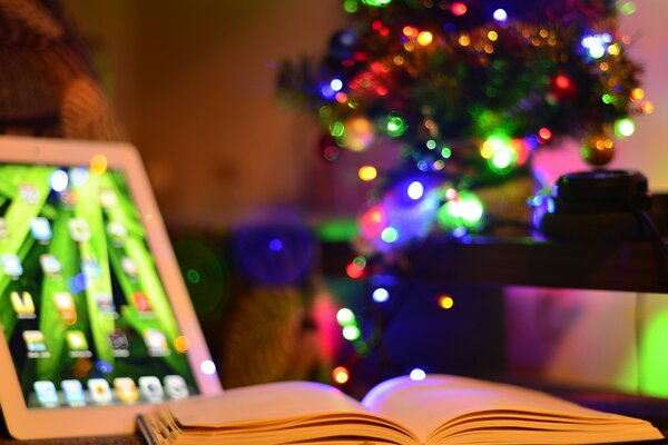 An open book and an iPad on the background of a Christmas tree