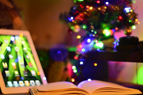 Раскрытая книга и айпад на, фоне новогодней елки