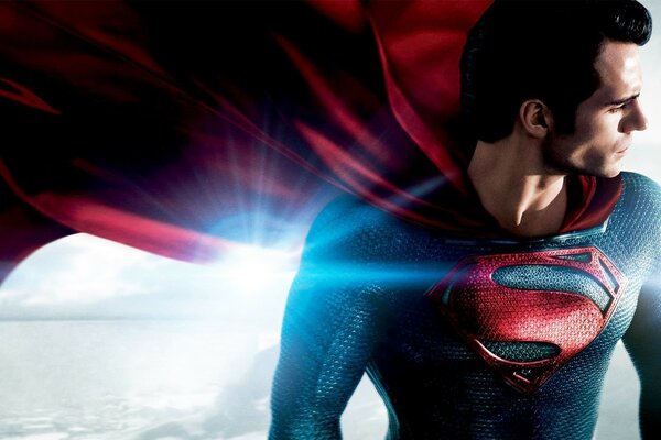 A man in a superman suit with a fluttering red cape on a bright light looks away
