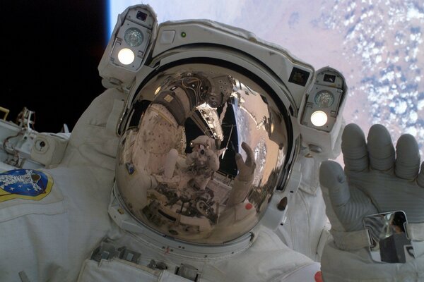 An astronaut in orbit in space is reflected in a spacesuit