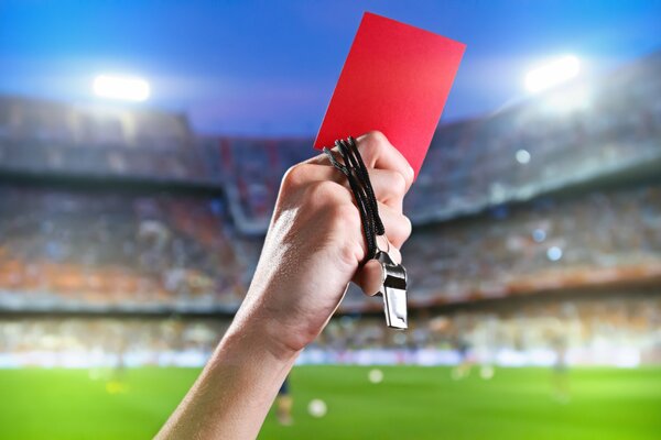 Main d un arbitre de football avec un carton rouge et un sifflet