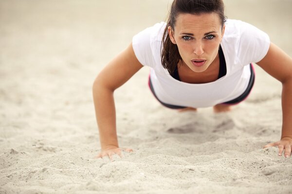 Женщина делает отжимания на песке