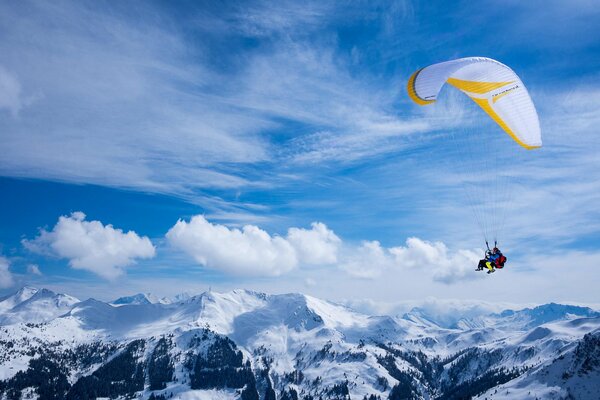 The paraglider flies over the snowy peaks