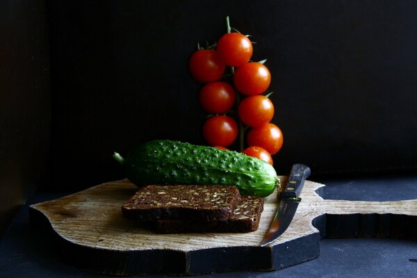 Cibo su una tavola con un coltello e pane con verdure pomodori e cetriolo