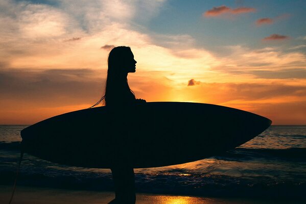 Silueta de una niña con una tabla de surf en el fondo del mar y una lujosa puesta de sol