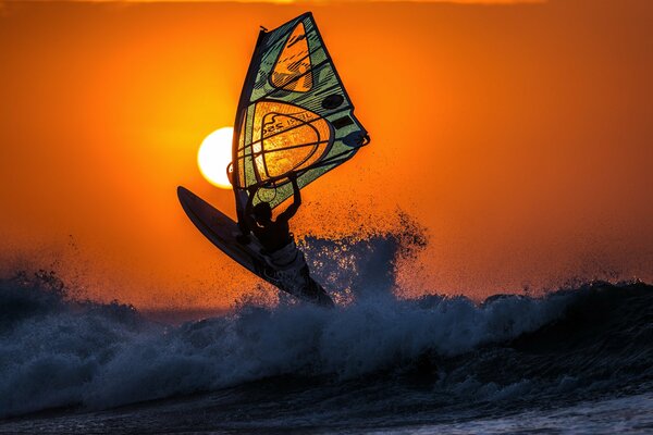 Surfen Sie bei Sonnenuntergang im Meer durch die Wellen