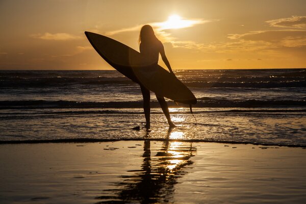 Девушка стоит на песке у моря с доской