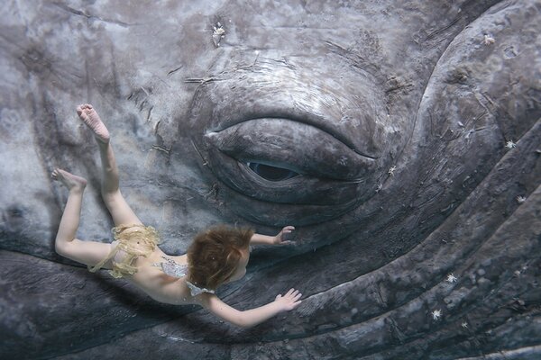 Un niño bajo el agua cerca de un enorme ojo de una criatura desconocida