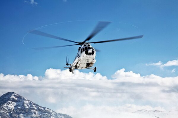 Вертолёт летит в воздухе над облаками и горами
