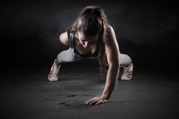 A sporty girl with her hair pulled back does push-ups on one hand