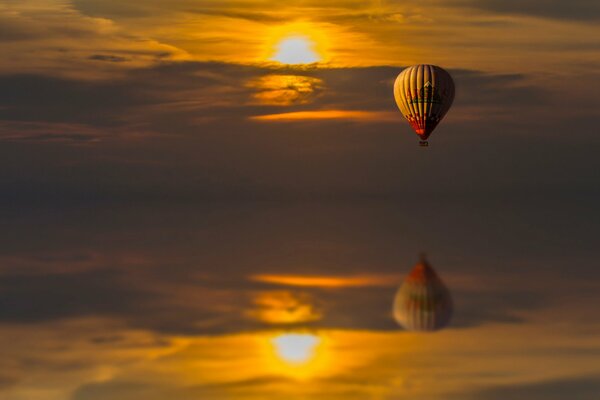 Reflection in the water of a balloon flying at sunset