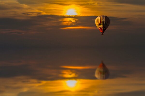 Reflejo en el agua de un globo que vuela al atardecer