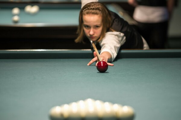 The girl aims the cue at the ball