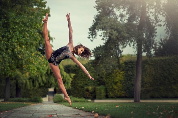 A gymnast girl in a jump does the splits in the park