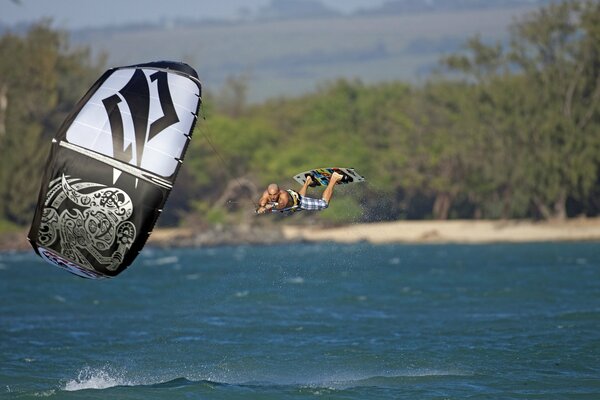 Surfer flies over the sea, holding on to a parachute