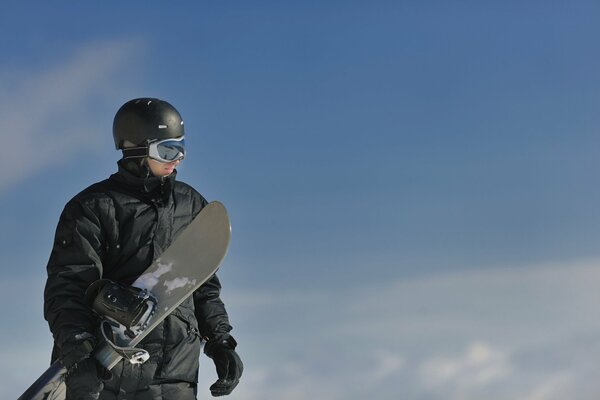 A snowboarder stands with a snowboard against the sky