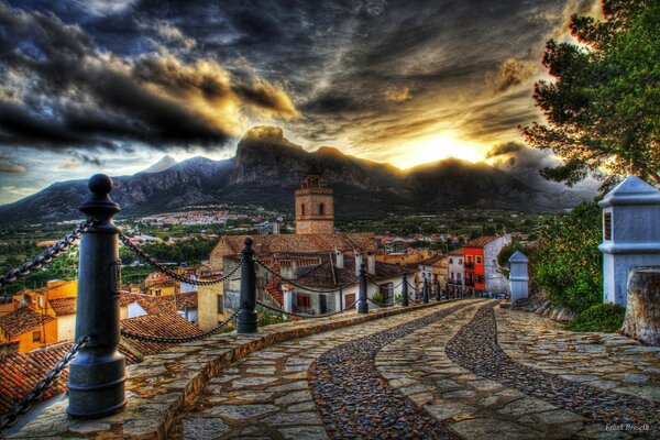 The cobblestone road descends to the town