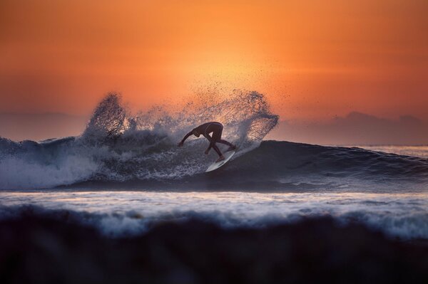 Surfista cabalga sobre una tabla en medio de una puesta de sol