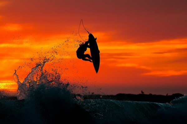 Surfista vuela sobre una ola al atardecer