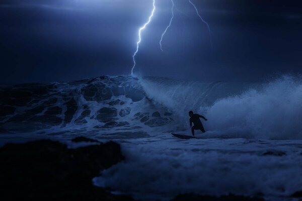 El chico está surfeando, conquistando una Ola por la noche en el océano en una tormenta eléctrica