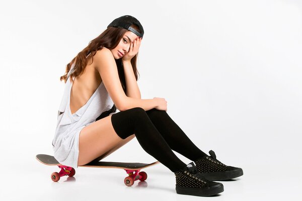 A girl in black knee socks is sitting on a skateboard