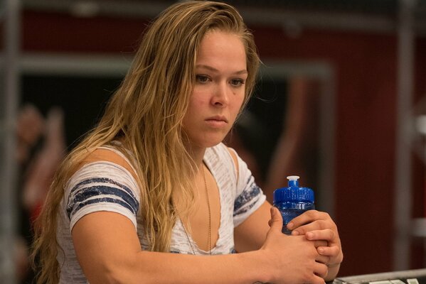 Photo du lutteur américain Ronda rousey dans un t-shirt blanc, avec une bouteille d eau bleue à la main