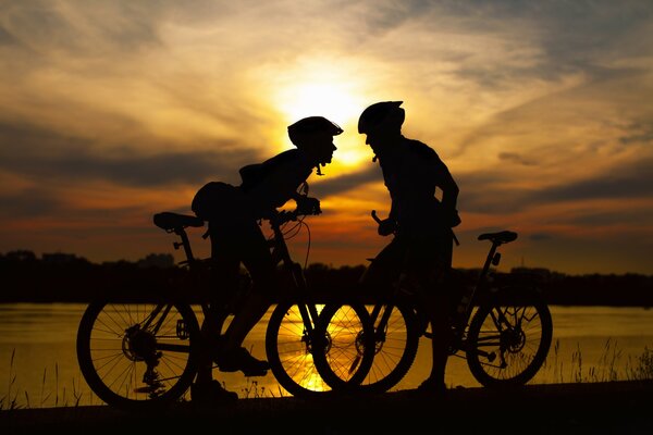 2 cyclists on the background of sunset and river