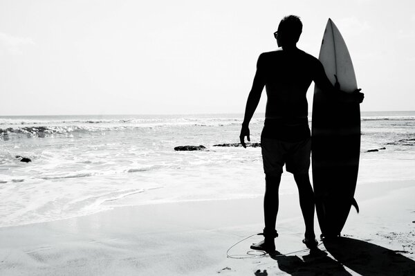 Schwarz-Weiß-Foto eines Surfers mit einem Brett am Strand