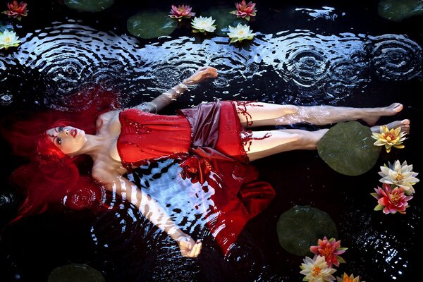 A girl with red hair lies in the water with water lilies