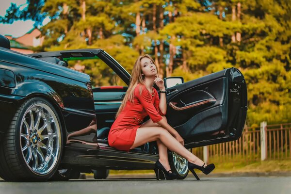 A girl in a red dress is sitting at the open car door