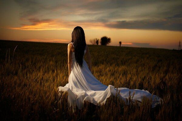 A girl in a white dress in a field at sunset