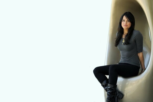Michelle Rodriguez is sitting in jeans and boots on a chair