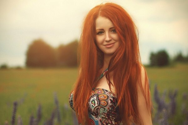 Piękna dziewczyna z długimi rudymi włosami, z eleganckim uśmiechem, na tle pola