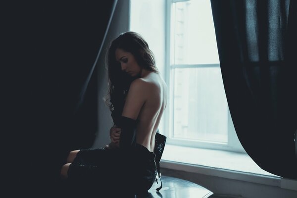 Młoda dziewczyna siedzi przy oknie z nagimi plecami