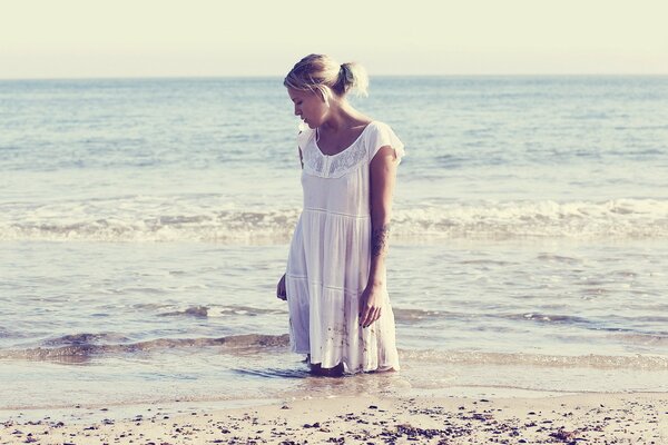 Una chica con un vestido blanco posa en el fondo de las olas del mar