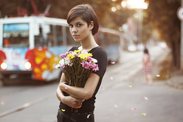 Кареглазая девушка с цветами посередине шумного города