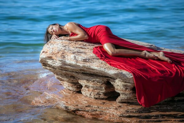 Una chica con un vestido rojo en una roca contra el mar