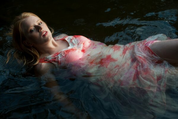 Red-haired girl in a wet dress on the background of a stream