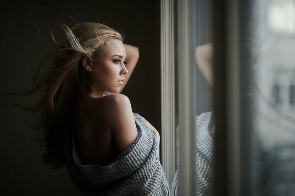 Mädchen mit blonden Haaren schaut aus dem Fenster