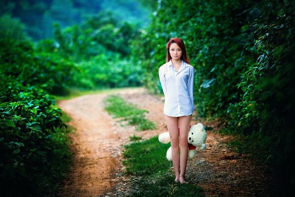 An Asian woman is standing on the road with a bear in her hands