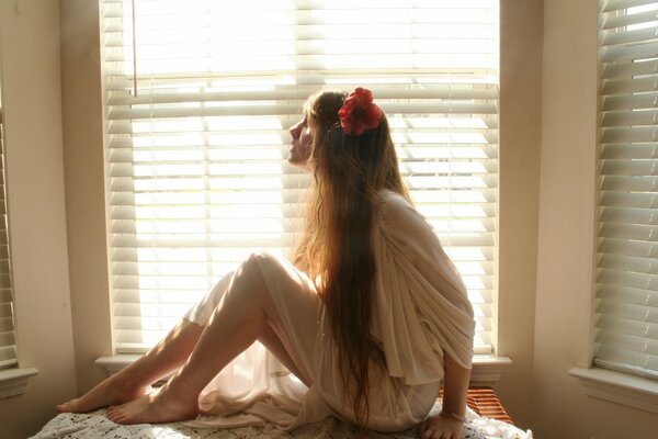 The girl is sitting by the window barefoot